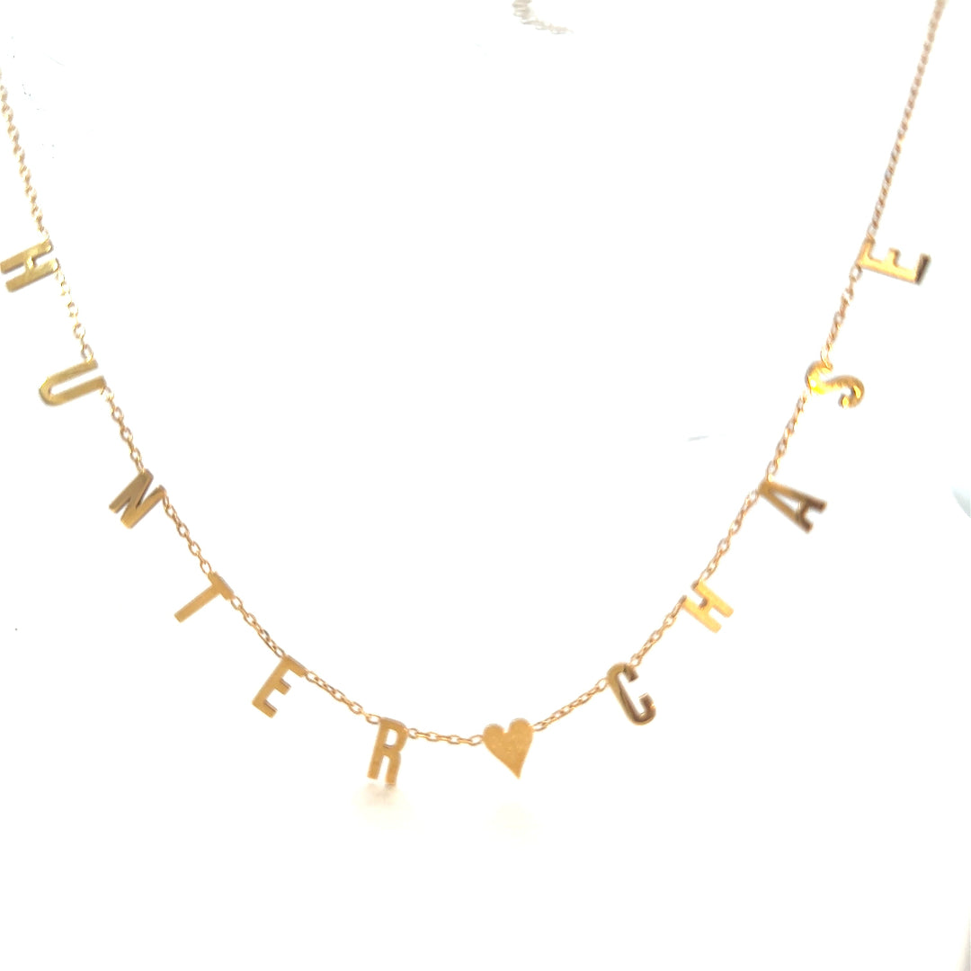Gold necklace with heart and letter charms on a white background